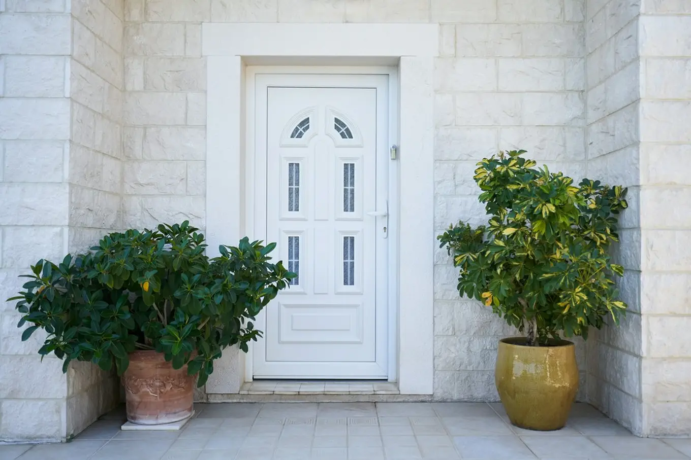 białe drzwi wejściowe i dwie donice z kwiatami